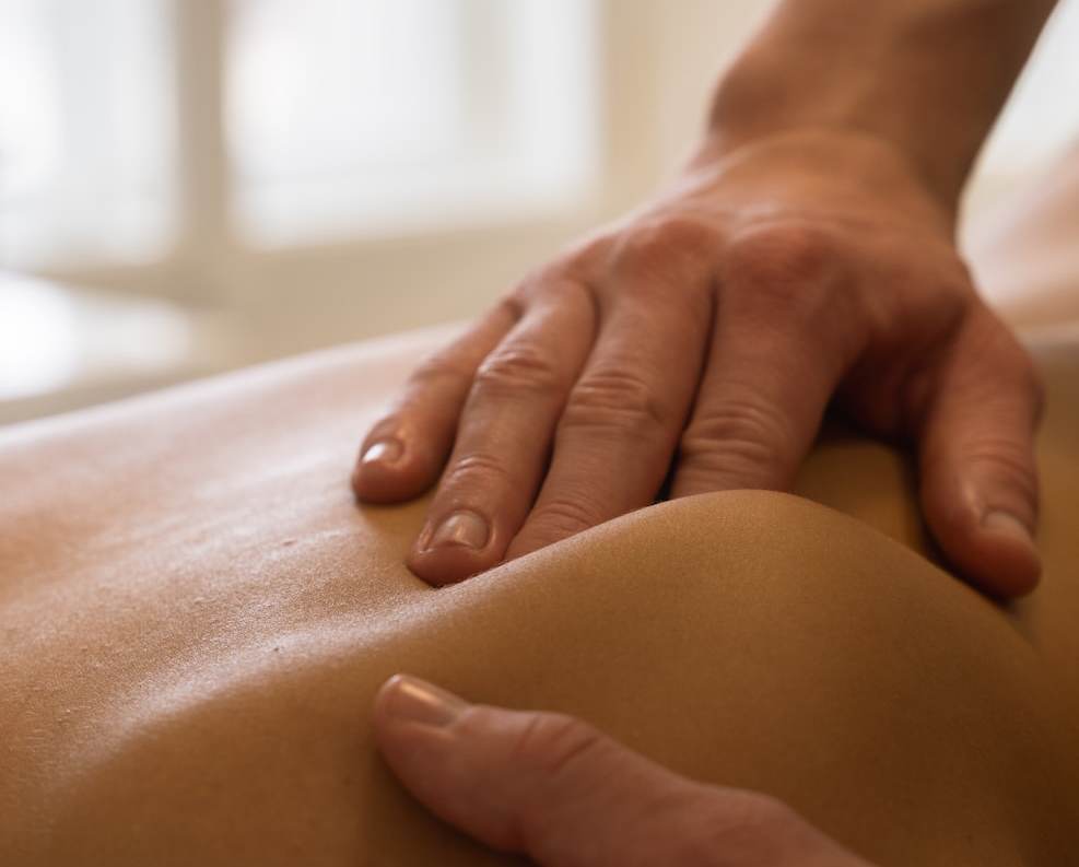 Close-up of a massage therapist's hands on a client's back during a session in a bright treatment room