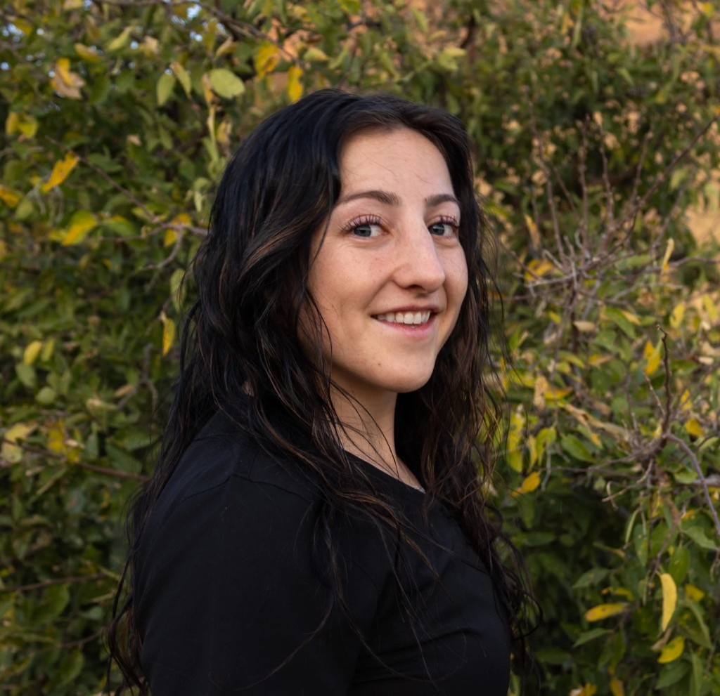 Portrait of Ashlyn, massage therapist at Lumen Hair Removal Clinic, smiling outdoors with green foliage behind her